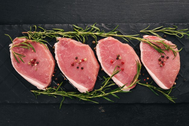 Raw meat Beef steak with rosemary and spices on a black wooden background Top view Free space for text