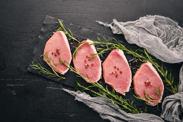 Raw meat Beef steak with rosemary and spices on a black wooden background Top view Free space for text