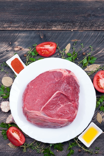 Raw meat beef with herbs, spices, olive oil and tomatoes on old wooden background