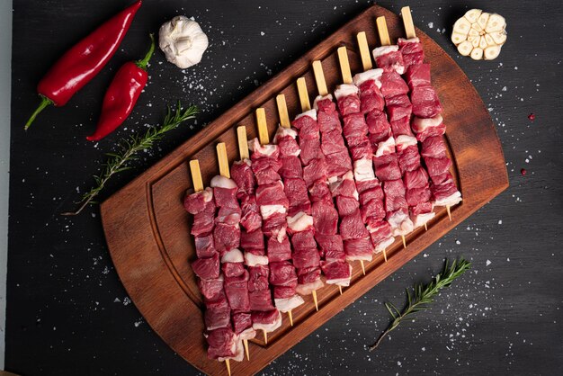 Raw meat on black background. small pieces of raw meat on\
wooden skewers