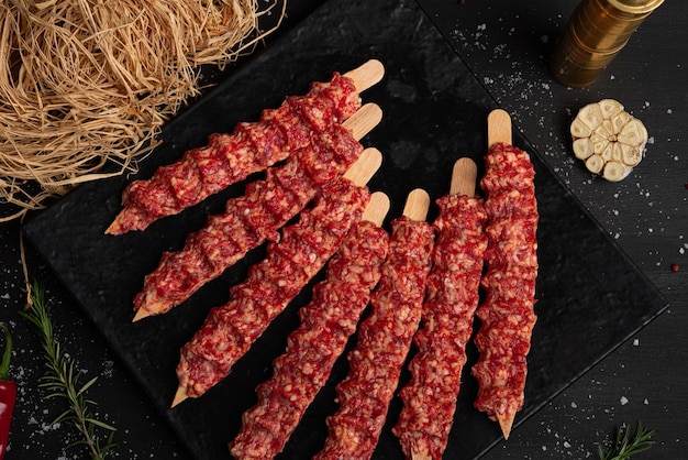 Raw meat on black background. small pieces of raw minced meat\
on wooden skewers