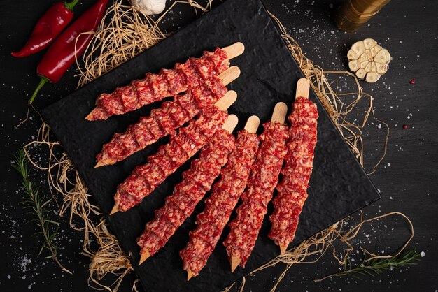 Raw meat on black background. Small pieces of raw minced meat on wooden skewers