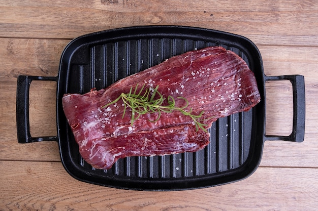 Raw meat in cast iron plate with rosemary branch on wooden table - top view