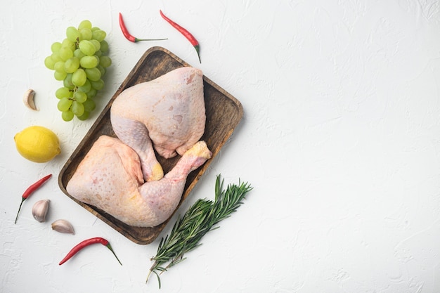 生肉。鶏の脚、ばち状核突起のカットセット、ブドウとパセリ、白いテーブル、上面図フラットレイ