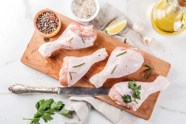 Raw meat, chicken legs, with olive oil, herbs and spices, on white marble background, copy space top view