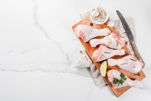 Photo raw meat, chicken legs, with olive oil, herbs and spices, on white marble background, copy space top view