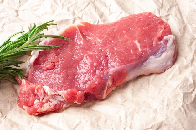 Raw meat Closeup slice of fresh juicy raw meat with rosemary on paper Preparing meat for a barbecue