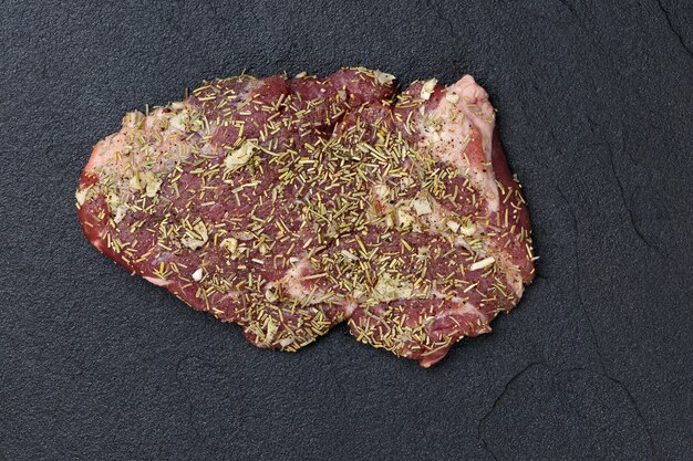 Raw meat on a dark background with spices prepared for grilling.