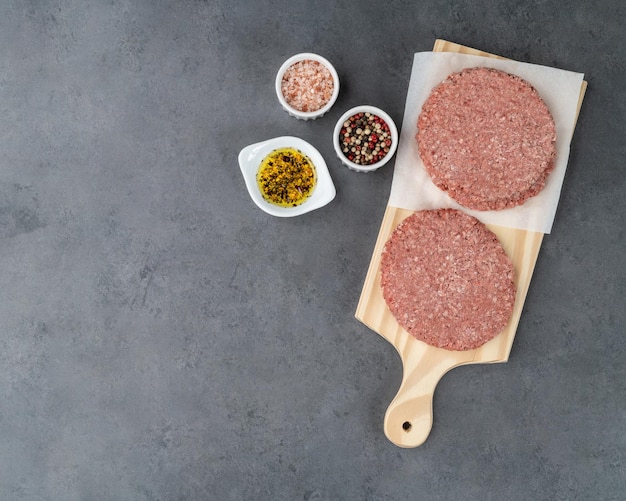 Raw meat hamburger over wooden board with seasonings and copy space.