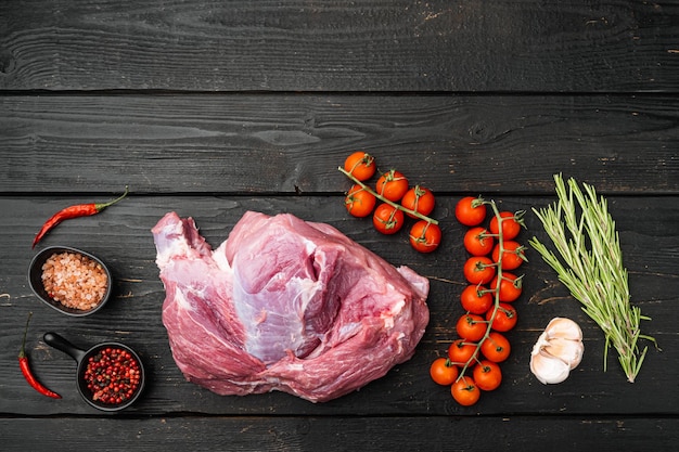 Carne cruda, pezzo di maiale con set di condimenti, su sfondo di tavolo in legno nero, vista dall'alto piatta, con spazio di copia per il testo