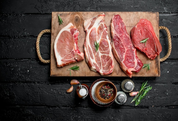 Raw meat Pork and beef steaks on a tray with spices and rosemary sprig