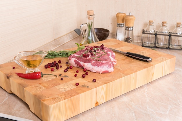 Carne cruda. bistecche di maiale su una tavola di legno con spezie, frutti di bosco, olio