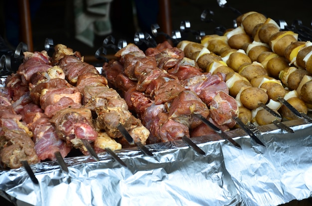 Raw meat and potatoes are planted on metal skewers. The process of cooking shish kebabs. Russian and Ukrainian camp food