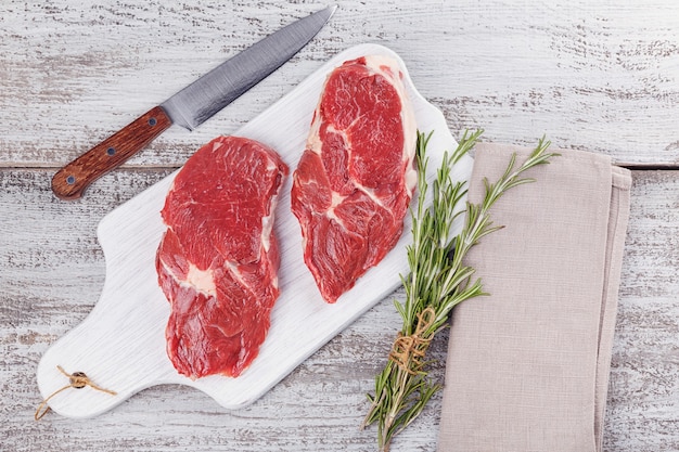 Raw meat. Raw beef steak on a white cutting board with rosemary. Flat lay