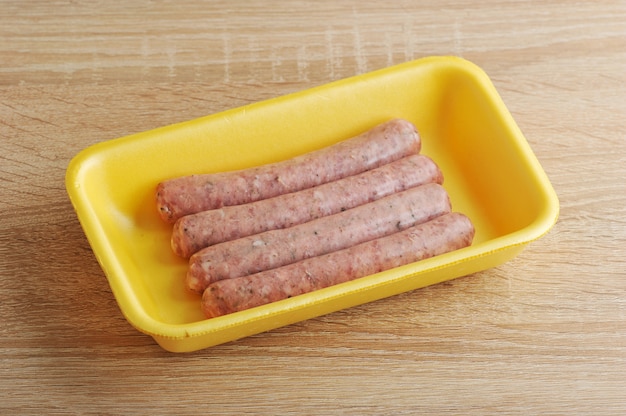 Raw meat sausages in a yellow plastic tray