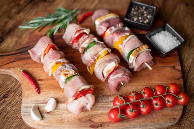 Raw meat skewers with vegetables on wooden background