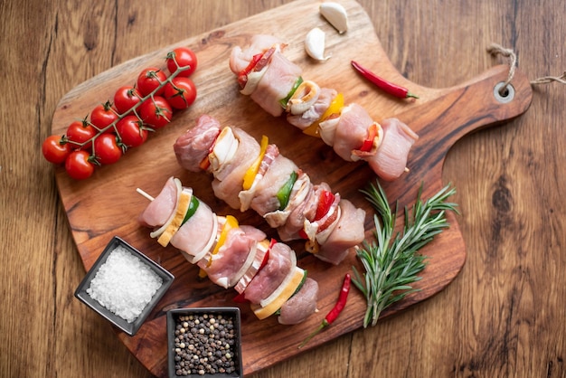 Raw meat skewers with vegetables on wooden background