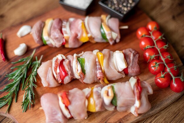 Raw meat skewers with vegetables on wooden background