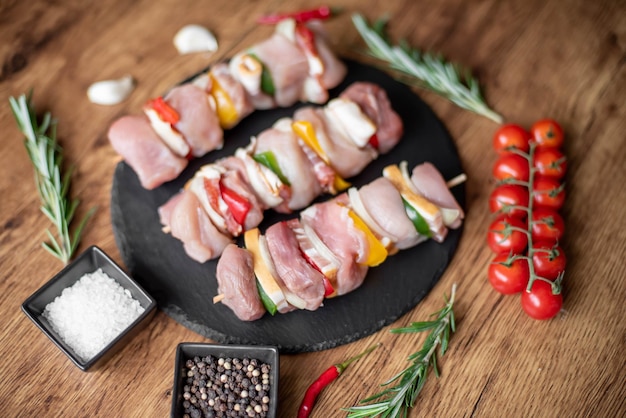 Raw meat skewers with vegetables on wooden background