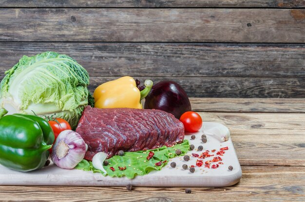 Raw meat, spices and vegetables on rustic wooden board