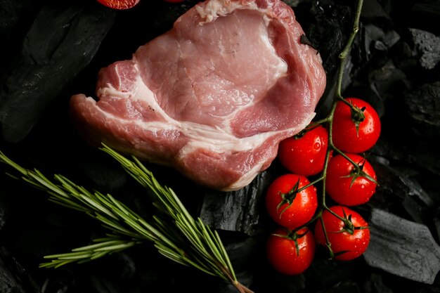 стейк из сырого мяса на фоне углей стейк из сырого мяса с помидорами черри и розмарином на углях