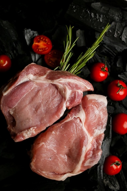 Raw meat steak on a background of charcoal raw steak with\
cherry tomatoes and rosemary on the coals