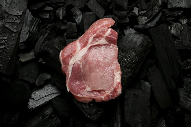 Raw meat steak on a black background of charcoal raw steak on\
the coals top view