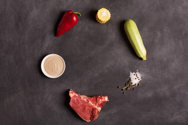 Raw meat steak on black chalkboard with vegetables