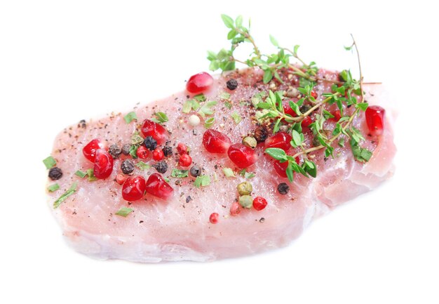 Raw meat steak with herbs spices and pomegranate seeds isolated on white