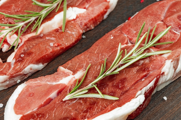 Raw meat steaks with herbs on wooden board