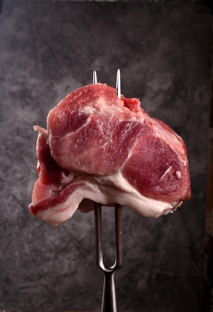 Carne cruda bloccata su una grande forchetta su sfondo nero