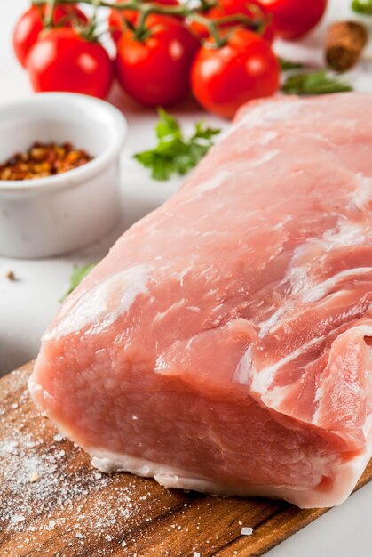 Raw meat with ingredients for dinner. Pork fillet, tenderloin, on cutting board, with salt, pepper, parsley, rosemary, oil, garlic, tomato, mushroom.Black stone table, copy space