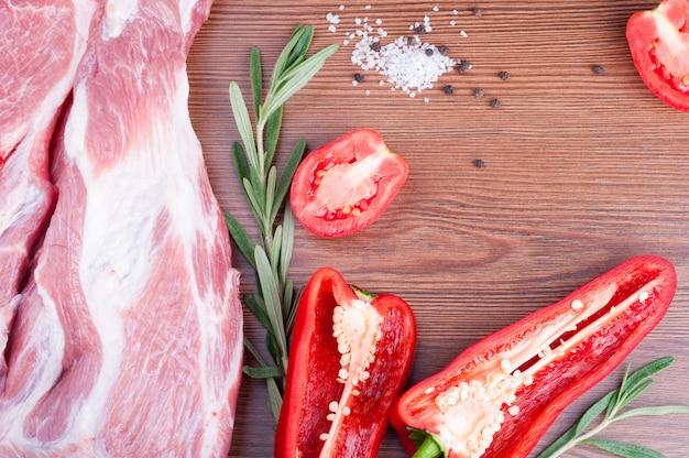 Raw meat with pepper, tomatoes, rosemary and spices on wooden table