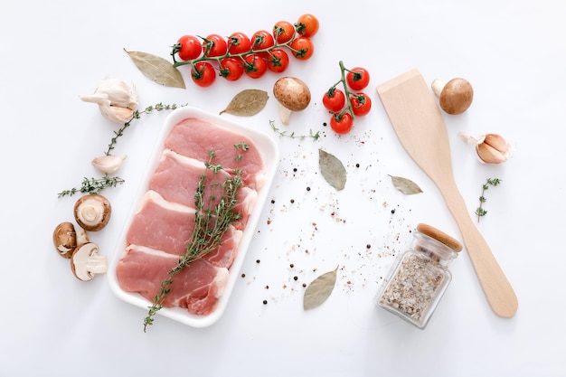 Raw meat and wooden spatula with different spices and vegetables on grey table background top view