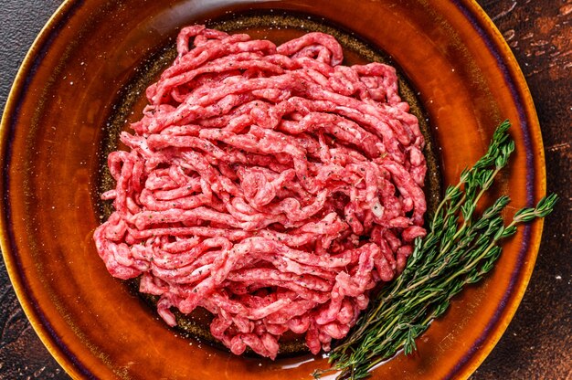 Raw mince angus wagyu beef, ground meat with herbs on a plate. Dark background. Top view.