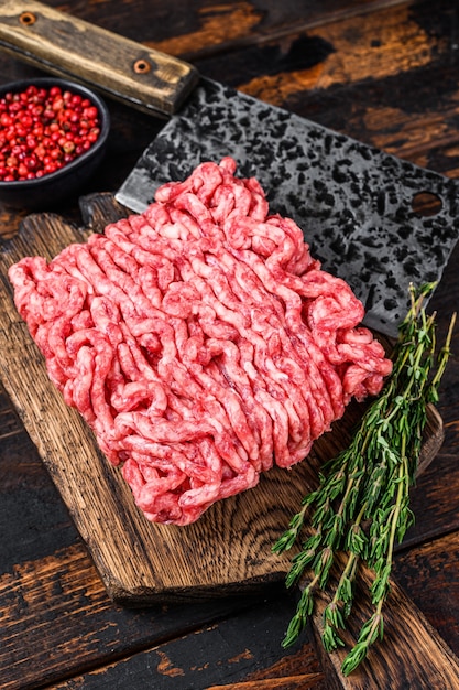 Raw mince beef, ground meat with herbs and spices on a wooden cutting board. Dark wooden background. Top view.