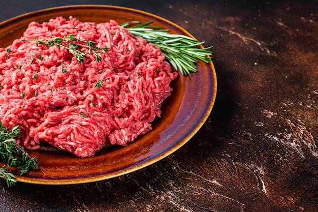 Raw mince beef and lamb meat on a rustic plate with herbs. Dark background. Top view. Copy space.