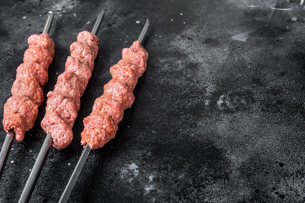 Raw mince lamb meat shish kebab on butcher table. Black background. Top view. Copy space.