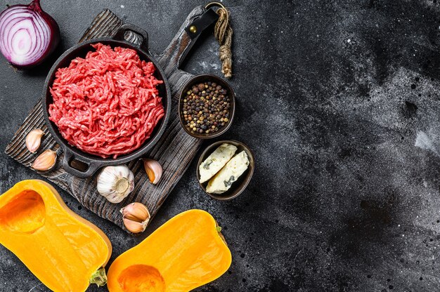 Raw mince meat, pumpkin with garlic and onion. Black background. Top view. Copy space.