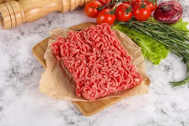Raw minced beef meat on cutting board with herbs and spices background