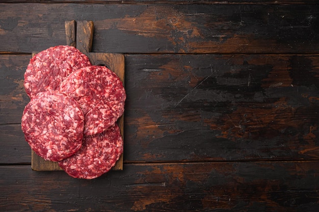 Cotolette di carne macinata cruda con set di erbe e spezie, su vecchio sfondo di tavolo in legno scuro, vista dall'alto piatta, con spazio per la copia per il testo