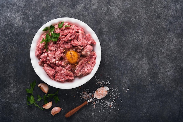 Raw minced meat Ground meat beef pork or lamb spices herbs and eggs on white plate on black old concrete background Fresh minced meat ready for cooking Food cooking background Top view