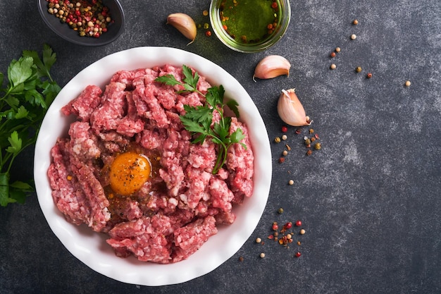 Carne macinata cruda carne macinata carne di maiale o agnello spezie erbe e uova su piatto bianco su sfondo nero vecchio cemento carne macinata fresca pronta per la cottura sfondo di cottura del cibo vista dall'alto