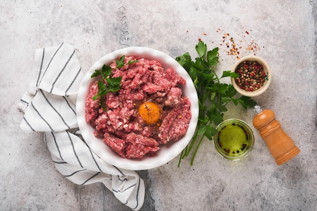 Raw minced meat ground meat beef pork or lamb spices herbs and\
eggs on white plate on light grey concrete background fresh minced\
meat ready for cooking food cooking background top view