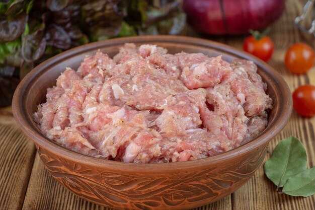 Raw minced pork in a plate and fresh vegetables on a table