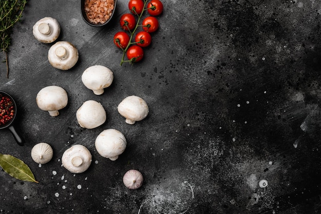 Set di mini funghi champignon crudi, su sfondo nero tavolo in pietra scura, vista dall'alto piatto, con spazio per la copia del testo