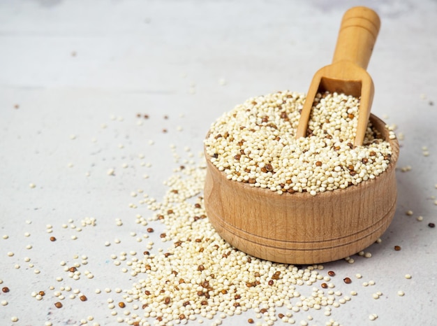 Raw mixed quinoa in bowl and scoop on light concrete background. Healthy and diet superfood