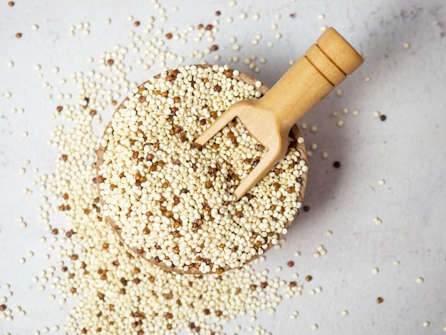 Raw mixed quinoa in bowl and scoop on light concrete background. Healthy and diet superfood