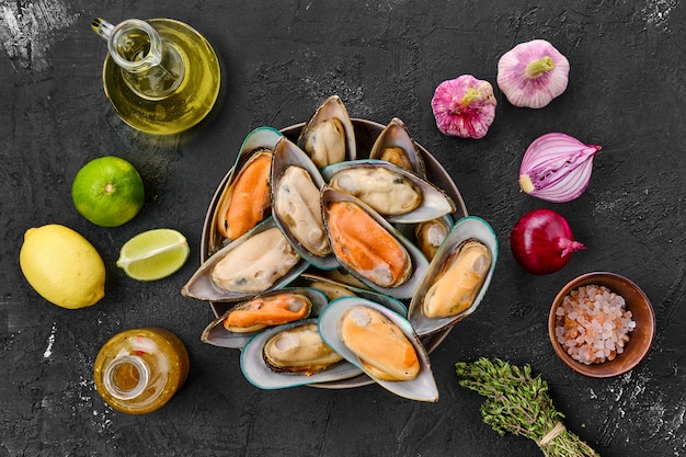 Raw mussels with spices and herbs on black table