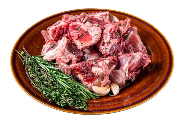 Фото Сырое мясо баранины, нарезанное кубиками для гуляша или тушеного мяса с костью на деревенской тарелке, изолированной на белом фоне